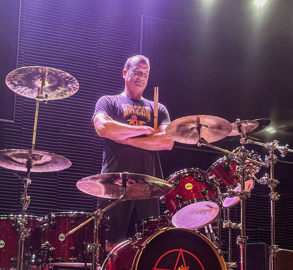 Matt Beeson standing behind his drumset in stage lighting.