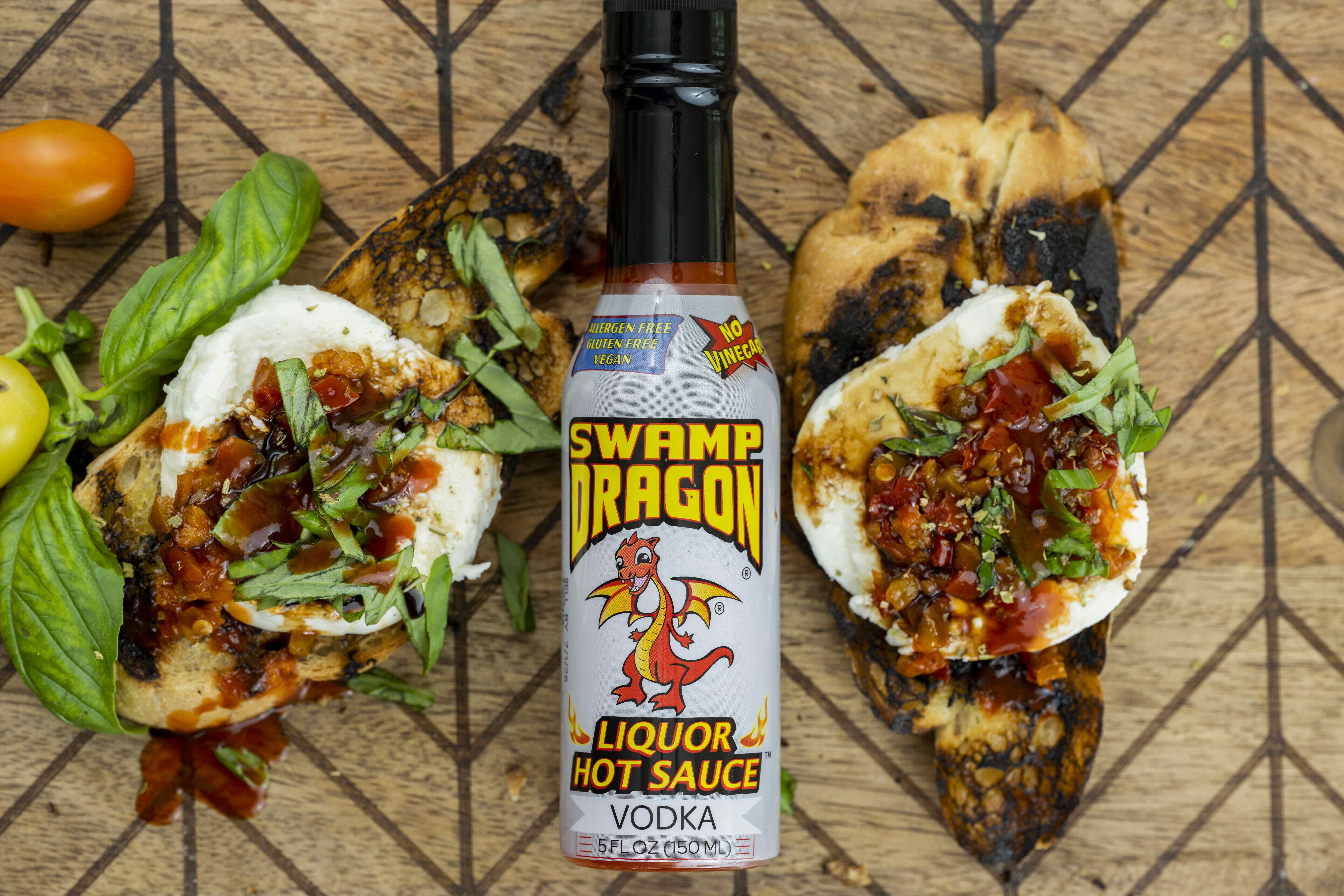 A bottle of Swamp Dragon Hot Sauce (the Vodka Dragon) placed between two pieces of grilled bruschetta